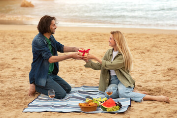 Boyfriend Giving Gift To Surprised Girlfriend While They Having Picnic On Beach