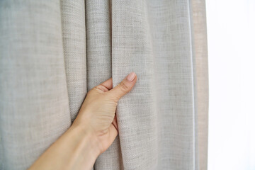 Fototapeta Light beige sand linen natural curtains on window, close-up of hand touching curtains obraz