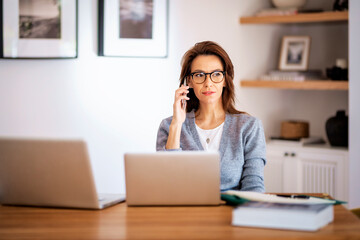 Mid aged business woman sitting at home and using laptops and having a call