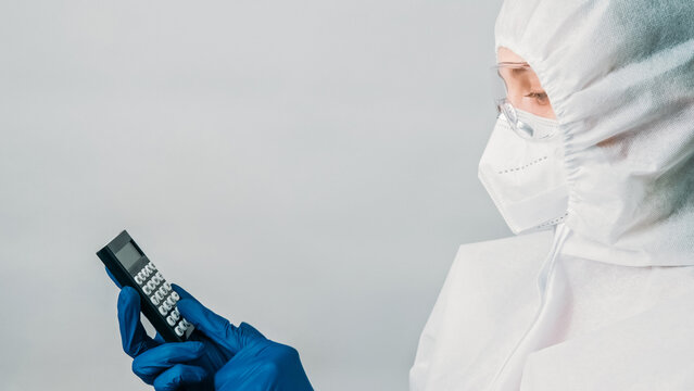 Medical calculations. Illness statistics. Nurse woman in protective suit mask counting number of cases isolated on grey background empty space.