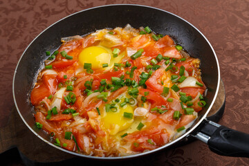 hot shakshuka in a frying pan sprinkled with green onions on a wooden board.