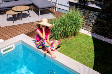 Happy woman wearing beachwear and sunglasses while relaxing by the poolside