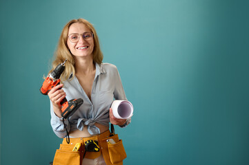 Young female worker with tool belt holding an electric screwdriver in hands isolated on background....