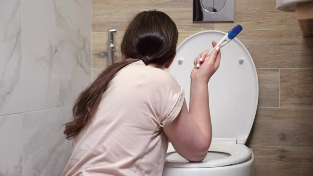 Expectant mother vomits sitting near light toilet bowl in bathroom. Toxicosis in pregnant female person. Violation of woman adaptation to pregnancy