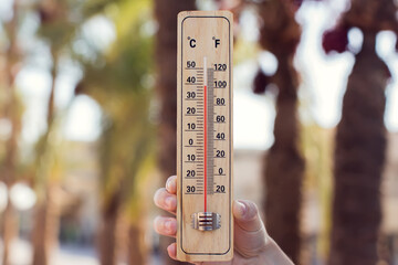 Hot weather. Thermometer in hand in front of street with trees and palms during heatwave. High temperature concept