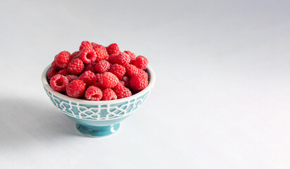 fresh raspberries in a blue bowl at the white table,summer harvest fresh berries