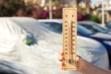 Hot weather. Thermometer in hand in front of covered car on tne street  during heatwave. High temperature concept