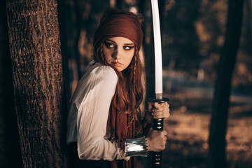 Outdoor portrait of young female in pirate costume with a sword.