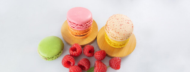 Colored macaron, French macaroon, French traditional cookies and raspberries on a light background. Dessert for tea, sweet breakfast