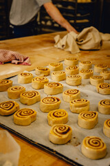 Cinnamon rolls sit on bakers tray in professional kitchen ready to be baked in the oven
