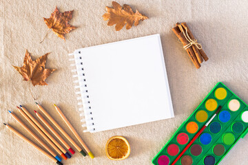 Autumn composition with blank sketchbook, watercolor palette, pencils, fallen dry leaves, cinnamon...