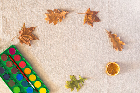 Autumn composition with a watercolor palette, fallen dry leaves lying in a circle on a background of linen fabric. Fall concept, Flat lay, top view, copy space
