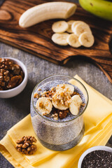 Chia seeds pudding with fresh banana and walnuts in a glass on the table vertical view