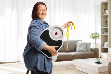 Overweight woman holding a weight scale and a measuring tape at home