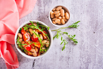 Appetizing salad of canned white beans, cherry tomatoes and arugula in a bowl top view