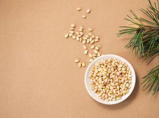 Pine nuts in a bowl on a yellow background with branches of pine needles. The concept of natural, organic and healthy superfoods and snacks.