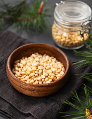 Pine nuts in a bowl and a jar on a dark background with branches of pine needles close up. The concept of a natural, organic and healthy superfood