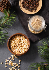 Fototapeta na wymiar Pine nuts in a jar, bowl and a scattered on a dark background with branches of pine needles and cone. The concept of a natural, organic and healthy superfood and snack.