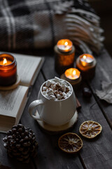 Aromatherapy on a grey fall morning, atmosphere of cosiness and relax. Autumn cozy home composition with hot chocolate with marshmallow and candles. Wooden background, books, close up.