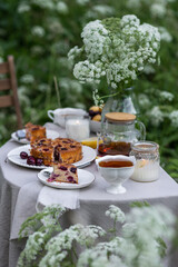 Fancy white porcelain set for herbal tea or coffee and homemade pie on wooden table in the garden. Summer outdoor party arrangement, romantic date. White flowers on background and in a glass vase