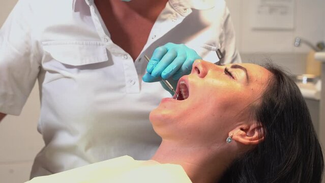 Dentist examining oral cavity mouth of the patient in dental chair with mirror and tools in medical office. Hygiene and health of oral teeth