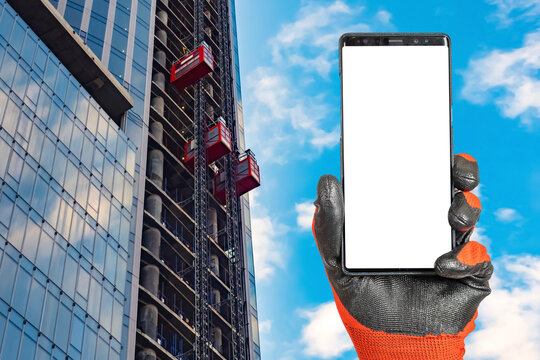 Phone in builder hand. Smartphone mock up. Skyscraper under construction. Elevators for construction work. Template for advertising construction services. Place for text on white phone display