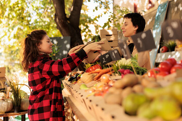 Organic food from farm. Young woman buying fresh herbs while shopping for local produce at farmers market. Female small business owner serving customer, selling home-grown fruits and vegetables