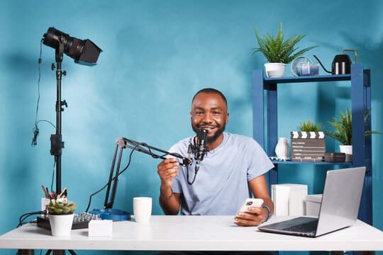 Smiling blogger reading engaging content on smartphone and looking at camera while recording video. Cheerful man sharing fun news and holding mobile phone while streaming live portrait