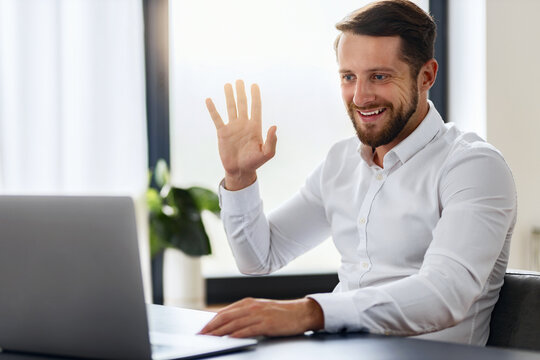 Smiling business, CEO, manager in white shirt showing a greeting sign having online conference with partners and employees sitting in the office