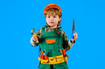 Little builder kid in safety helmet with saw and hammer. Little repairman or construction worker in overalls with toolbelt. Kid game. Cute child boy in hardhat and builder's uniform with instruments.