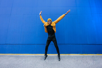 Fototapeta premium Funny African American man with yellow winter sport coat jumping high - blue background