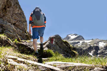 An athletic man with a backpack climbs a mountain trail against a cloudless sky, Austria