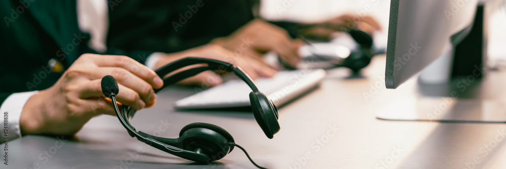 Aufkleber panorama focus hand holding headset on call center workspace desk with blur background of operator t