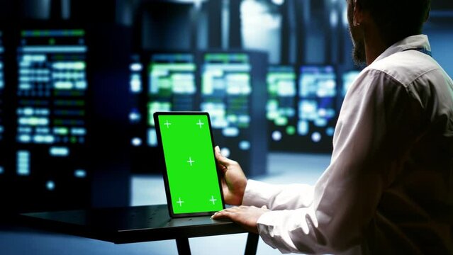 Specialist using green screen tablet to check server rigs doing intense computations. Technician preventing strain on data center equipment caused by AI applications driving up power usage