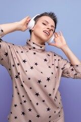 active bright caucasian young woman with a short haircut dressed in a beige suit listens to music...