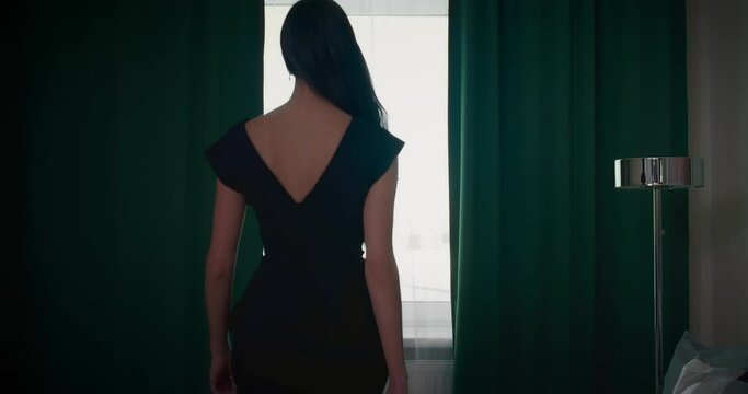 beautiful fashion model in black dress walking in room, looking at window, back view, 4K, Prores