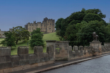 Obraz premium Looking at Alnwick Castle off a bridge with a lion statue