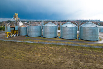 Flying a drone over silver silos on agro manufacturing plant for processing drying cleaning and storage of agricultural products, flour, cereals and grain. Large iron barrels of grain. aerial view