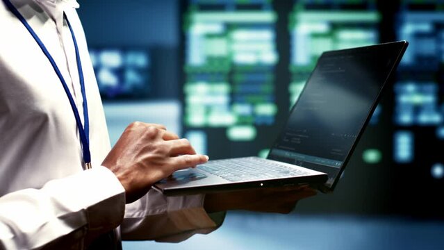 Close up of mechanic using laptop to check electronics in blockchain technology application specific integrated circuit server rig rows. Worker checking for issues in cryptocurrency mining farm