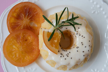 Orange bundt cake topped tangerines and rosemary on a white plate