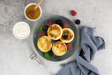 Cottage cheese pancakes, syrniki with sour cream, honey, berries on blue background. Top view. Russian, ukrainian food