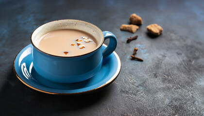 Indian masala chai, traditional spiced black tea with milk in blue cup on dark background....