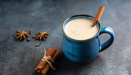 Indian masala chai, traditional spiced black tea with milk in blue cup on dark background. Horizontal orientation, selective focus