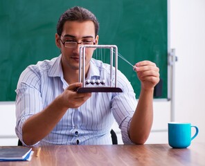 Young male teacher physicist in front of blackboard