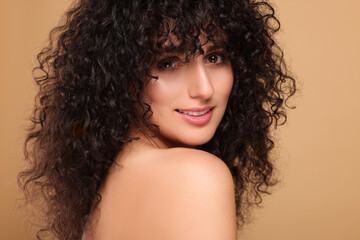 Beautiful young woman with long curly hair on beige background