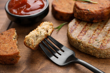 Fork with piece of delicious vegan cutlet on wooden table, closeup