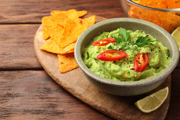 Bowl of delicious guacamole, lime and tortilla chips on wooden table, closeup. Space for text
