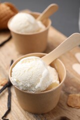 Paper cups with delicious ice cream and vanilla pods on wooden board, closeup