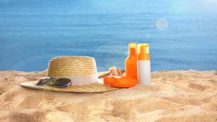Fototapeta na wymiar Hat with sunglasses and cosmetics on sunny ocean beach, banner design. Summer vacation