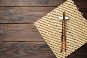 Bamboo mat with pair of chopsticks and rest on wooden table, top view. Space for text